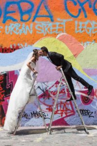 Jeunes mariés s'embrassant en haut des échelles devant un mur de graffitis